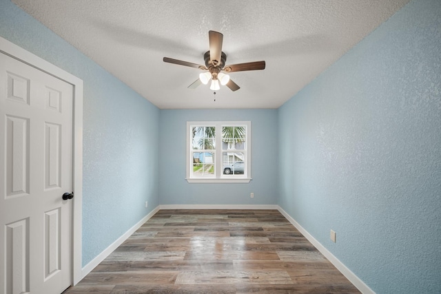 spare room featuring a textured wall, wood finished floors, baseboards, ceiling fan, and a textured ceiling