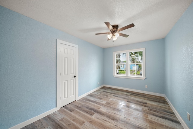 empty room featuring a textured wall, wood finished floors, baseboards, a textured ceiling, and a ceiling fan