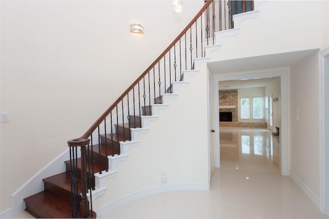staircase featuring a brick fireplace, a towering ceiling, and baseboards