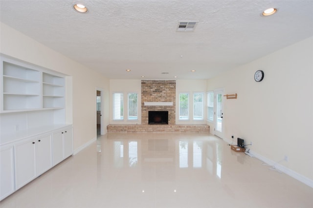 unfurnished living room with a brick fireplace, a textured ceiling, built in features, baseboards, and visible vents