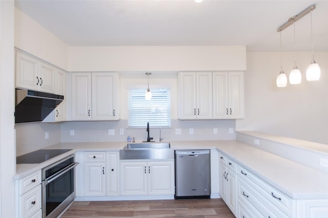 kitchen with a sink, light wood-style floors, a peninsula, appliances with stainless steel finishes, and ventilation hood
