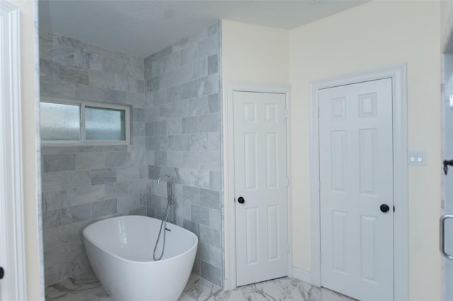 full bath with marble finish floor and a freestanding tub