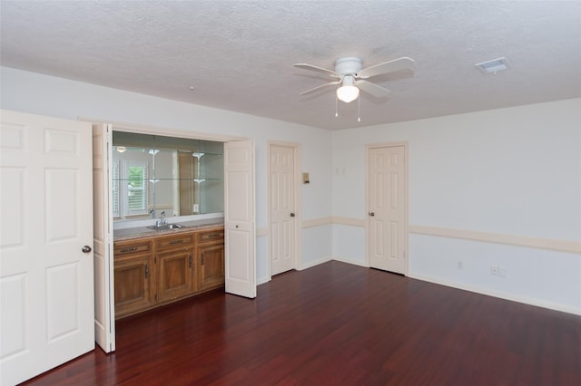 empty room featuring dark wood-type flooring, a textured ceiling, a sink, visible vents, and a ceiling fan