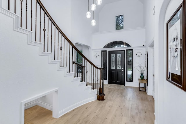 entrance foyer with stairs, light wood-style floors, baseboards, arched walkways, and a towering ceiling