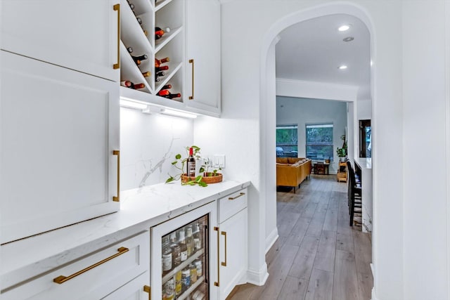 bar with wine cooler, decorative backsplash, arched walkways, a dry bar, and light wood-style flooring