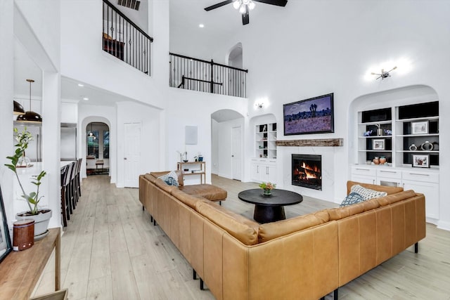 living area with a warm lit fireplace, a ceiling fan, arched walkways, and light wood-style flooring