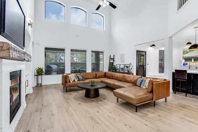 living area featuring a fireplace, light wood-style flooring, a ceiling fan, and a wealth of natural light