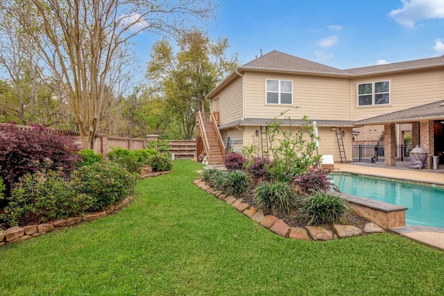 rear view of house with stairway, fence, a patio, a fenced in pool, and a lawn