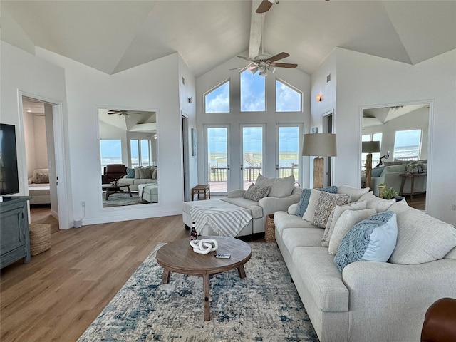 living room with a ceiling fan, high vaulted ceiling, light wood-style floors, and baseboards