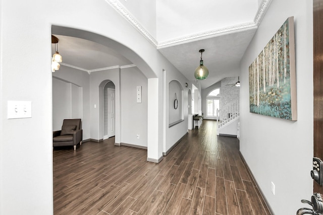 hallway with crown molding, stairway, dark wood finished floors, baseboards, and arched walkways