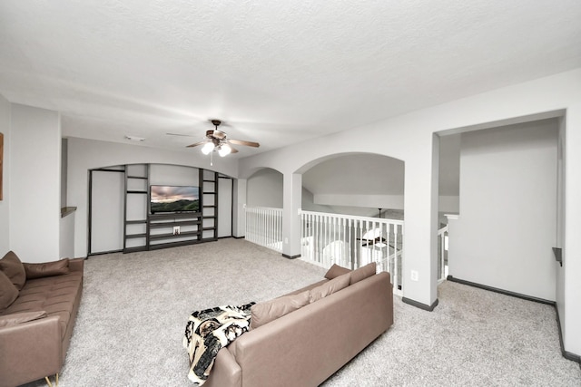 living room featuring a textured ceiling, baseboards, ceiling fan, arched walkways, and carpet floors