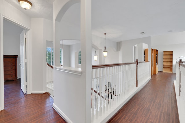 corridor featuring arched walkways, baseboards, visible vents, and wood finished floors