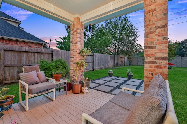 patio terrace at dusk with a lawn, an outdoor living space, and a fenced backyard