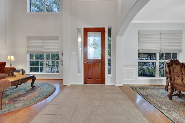 tiled entrance foyer featuring arched walkways, a towering ceiling, baseboards, and ornamental molding