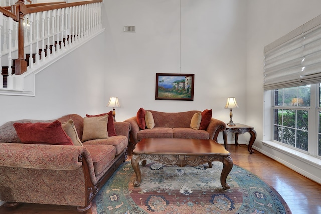 living room with stairs, a high ceiling, wood finished floors, baseboards, and visible vents