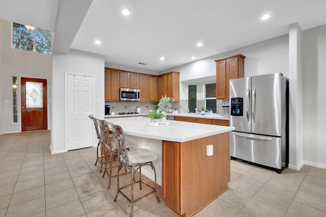 kitchen featuring light countertops, backsplash, a kitchen island, appliances with stainless steel finishes, and brown cabinetry