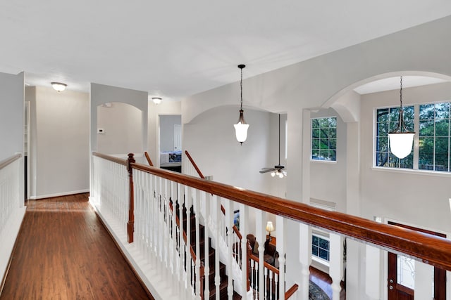 corridor with plenty of natural light, arched walkways, baseboards, and wood finished floors