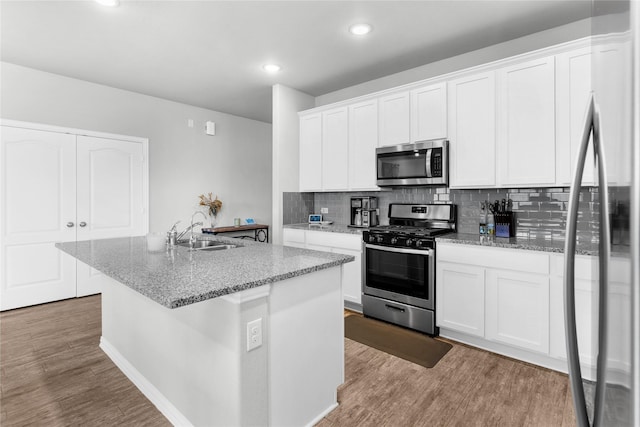 kitchen featuring white cabinetry, tasteful backsplash, a sink, light wood-style flooring, and appliances with stainless steel finishes