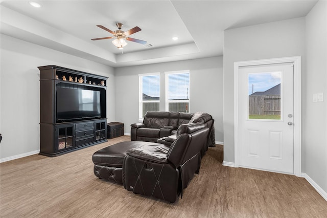 living area featuring baseboards, a tray ceiling, wood finished floors, and a ceiling fan