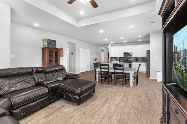 living room featuring baseboards, recessed lighting, a ceiling fan, a raised ceiling, and light wood-type flooring