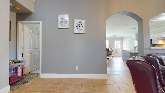 hallway featuring baseboards, arched walkways, ornamental molding, and light tile patterned floors