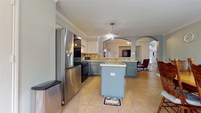 kitchen with light countertops, light tile patterned floors, backsplash, arched walkways, and black range with gas stovetop