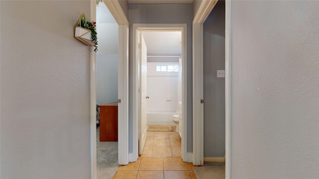 hallway featuring light tile patterned flooring, a textured wall, and baseboards