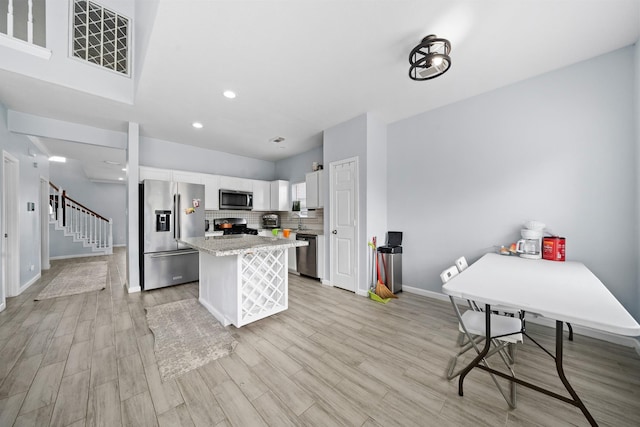 13619 Bonilla Ln, Houston, TX 77083 - kitchen with backsplash, a kitchen island, light wood finished floors, appliances with stainless steel finishes, and white cabinets