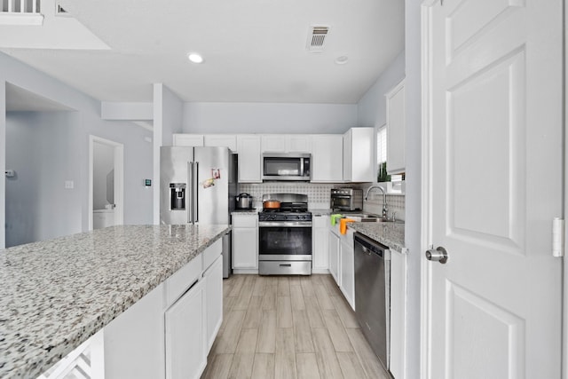 13619 Bonilla Ln, Houston, TX 77083 - kitchen with white cabinets, visible vents, stainless steel appliances, tasteful backsplash, and light stone counters