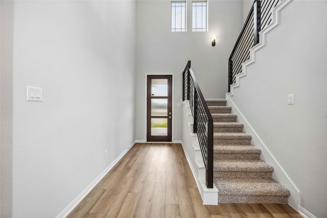 foyer with baseboards, a high ceiling, light wood-style flooring, and stairway
