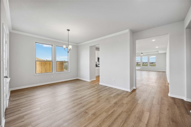 spare room featuring crown molding, baseboards, light wood-style floors, and a wealth of natural light