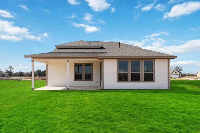 rear view of house with a shingled roof, a patio, and a yard