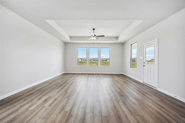 unfurnished room with a ceiling fan, a tray ceiling, baseboards, and wood finished floors
