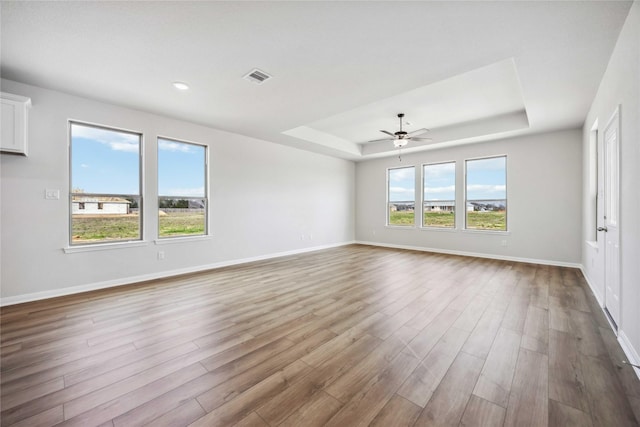 spare room featuring a tray ceiling, baseboards, visible vents, and wood finished floors
