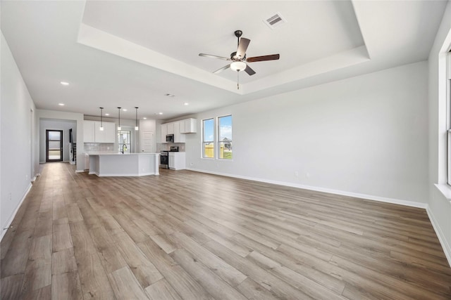 unfurnished living room featuring light wood-type flooring, a tray ceiling, and visible vents