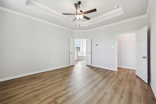unfurnished bedroom with a tray ceiling, baseboards, crown molding, and wood finished floors