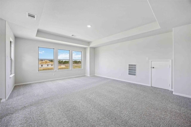 empty room with carpet flooring, a tray ceiling, baseboards, and visible vents