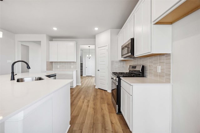 kitchen featuring light countertops, light wood-style flooring, stainless steel appliances, white cabinetry, and a sink
