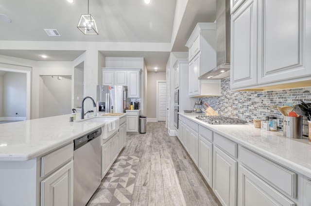 17473 Chestnut Cove Dr, Conroe, TX 77302 - kitchen featuring stainless steel appliances, wall chimney range hood, a sink, white cabinetry, and decorative backsplash