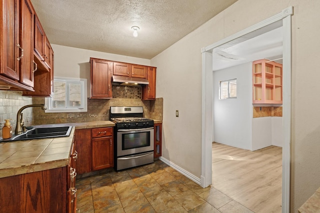 413 Mulcahy St, Rosenberg, TX 77471 - kitchen with tile counters, gas stove, under cabinet range hood, a sink, and backsplash