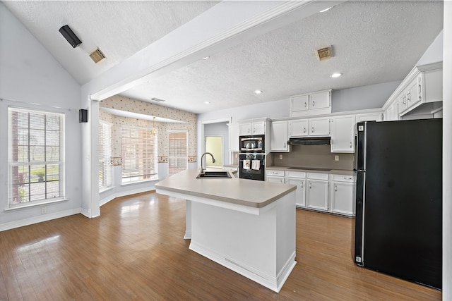 kitchen featuring light countertops, dark wood-type flooring, under cabinet range hood, visible vents, and black appliances