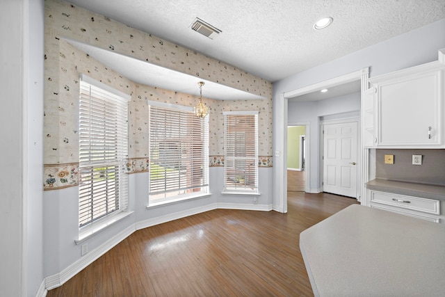 unfurnished dining area featuring baseboards, wallpapered walls, visible vents, and wood finished floors