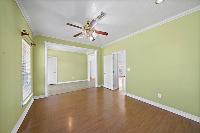 empty room with crown molding, baseboards, ceiling fan, visible vents, and wood finished floors