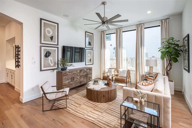 living room with light wood-type flooring, a healthy amount of sunlight, baseboards, and a ceiling fan