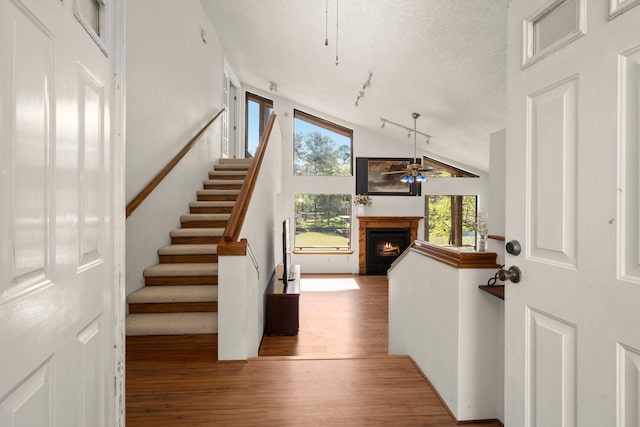 foyer entrance featuring stairs, a ceiling fan, a warm lit fireplace, wood finished floors, and a textured ceiling