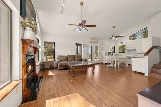living area featuring plenty of natural light, light wood finished floors, a wall unit AC, and a glass covered fireplace