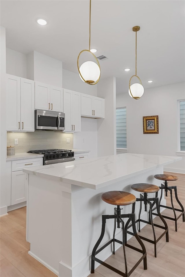 kitchen with white cabinets, stainless steel appliances, light stone counters, and light wood-style floors