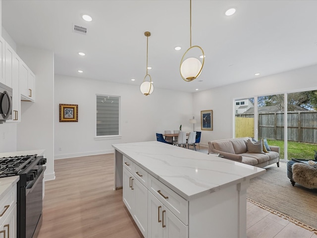 kitchen with visible vents, a kitchen island, light wood-style floors, open floor plan, and range with gas cooktop