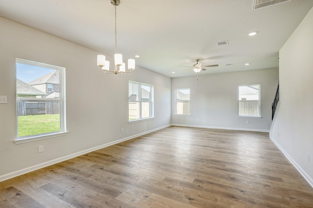empty room featuring baseboards, visible vents, wood finished floors, and ceiling fan with notable chandelier