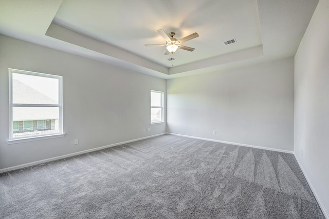 carpeted empty room featuring a raised ceiling, baseboards, ceiling fan, and visible vents